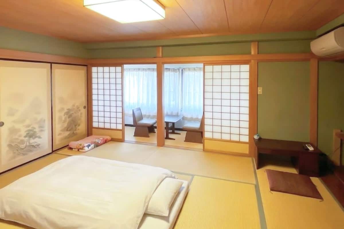 Una habitación japonesa tradicional con suelo de tatami, una cama, puertas correderas y vistas a través de un biombó shoji.