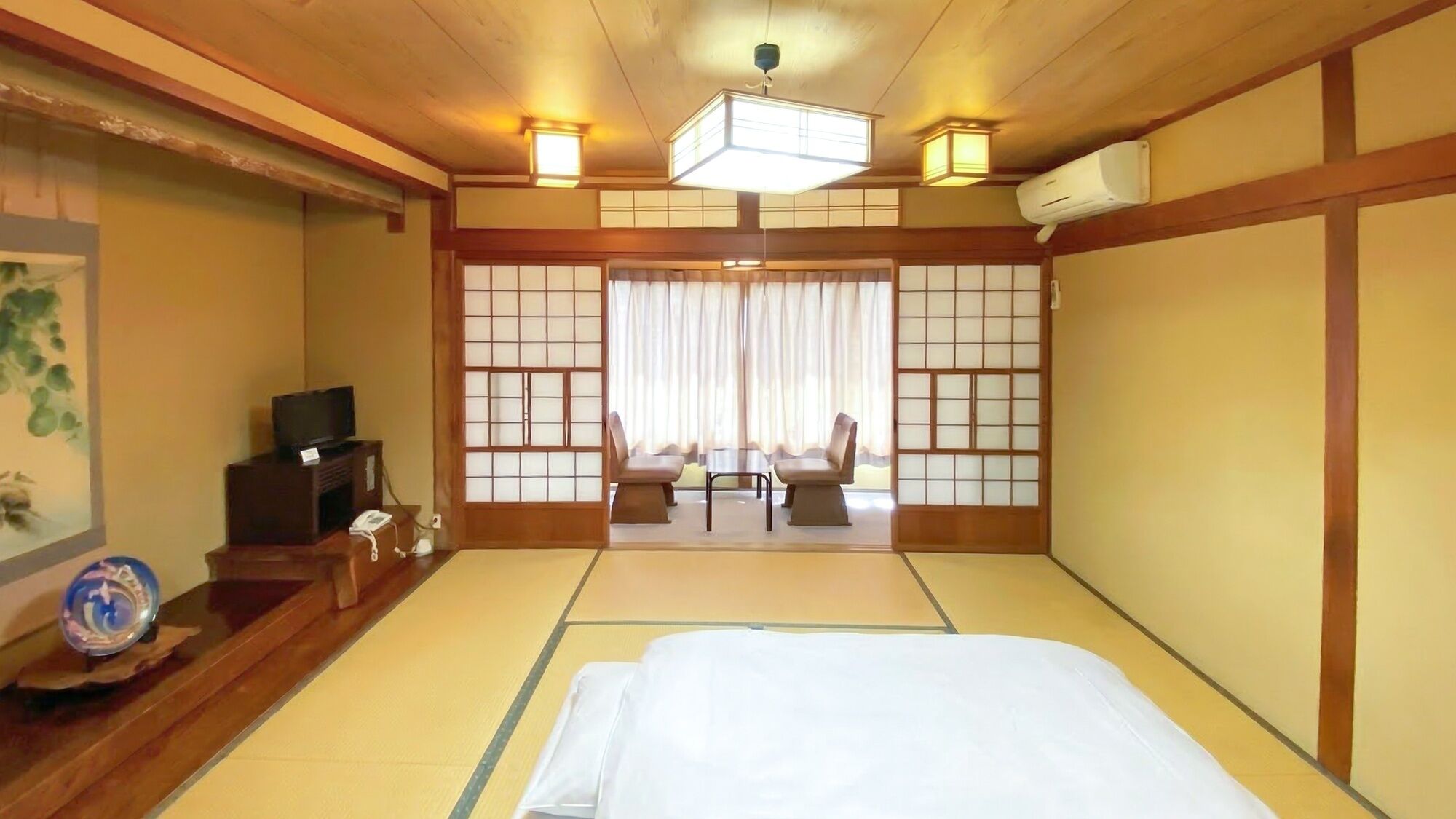 Perinteinen japanilaistyylinen huone, jossa on tatamimatto, sänky, televisio ja liukuovi, josta on näkymä parvekkeelle.