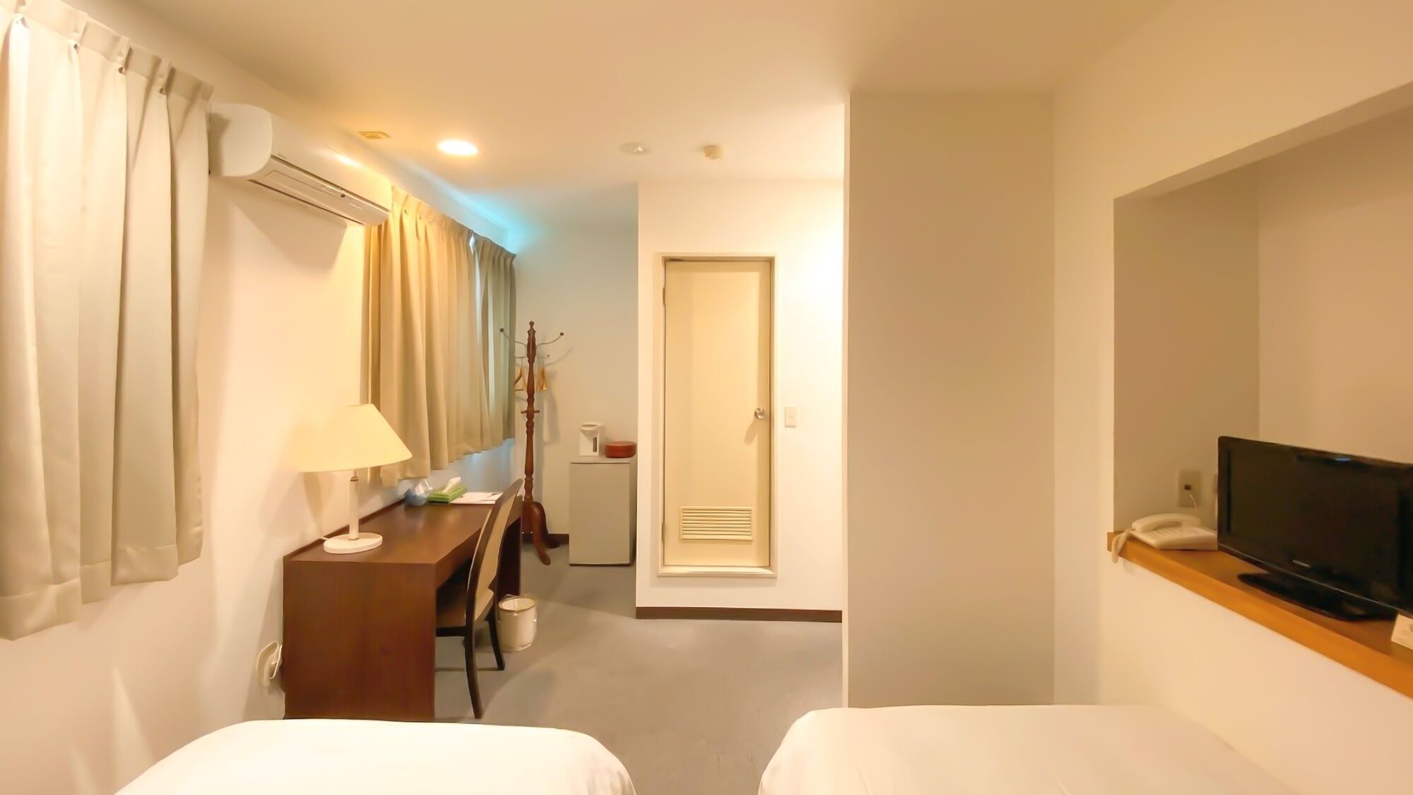 Hotellihuone, jossa on kaksi sänkyä, työpöytä lampun kanssa, televisio ja naulakko.
