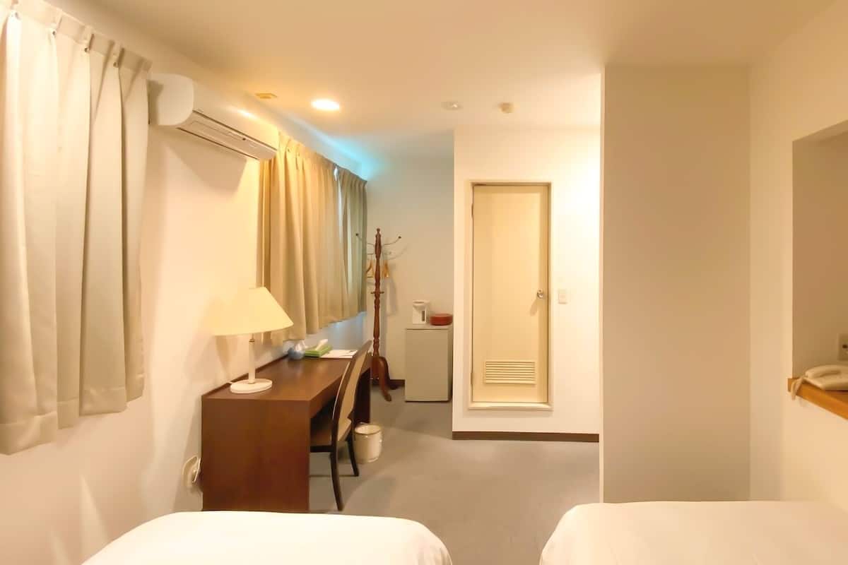 Quarto de hotel com duas camas, uma escrivaninha com luminária, uma televisão e um cabideiro.