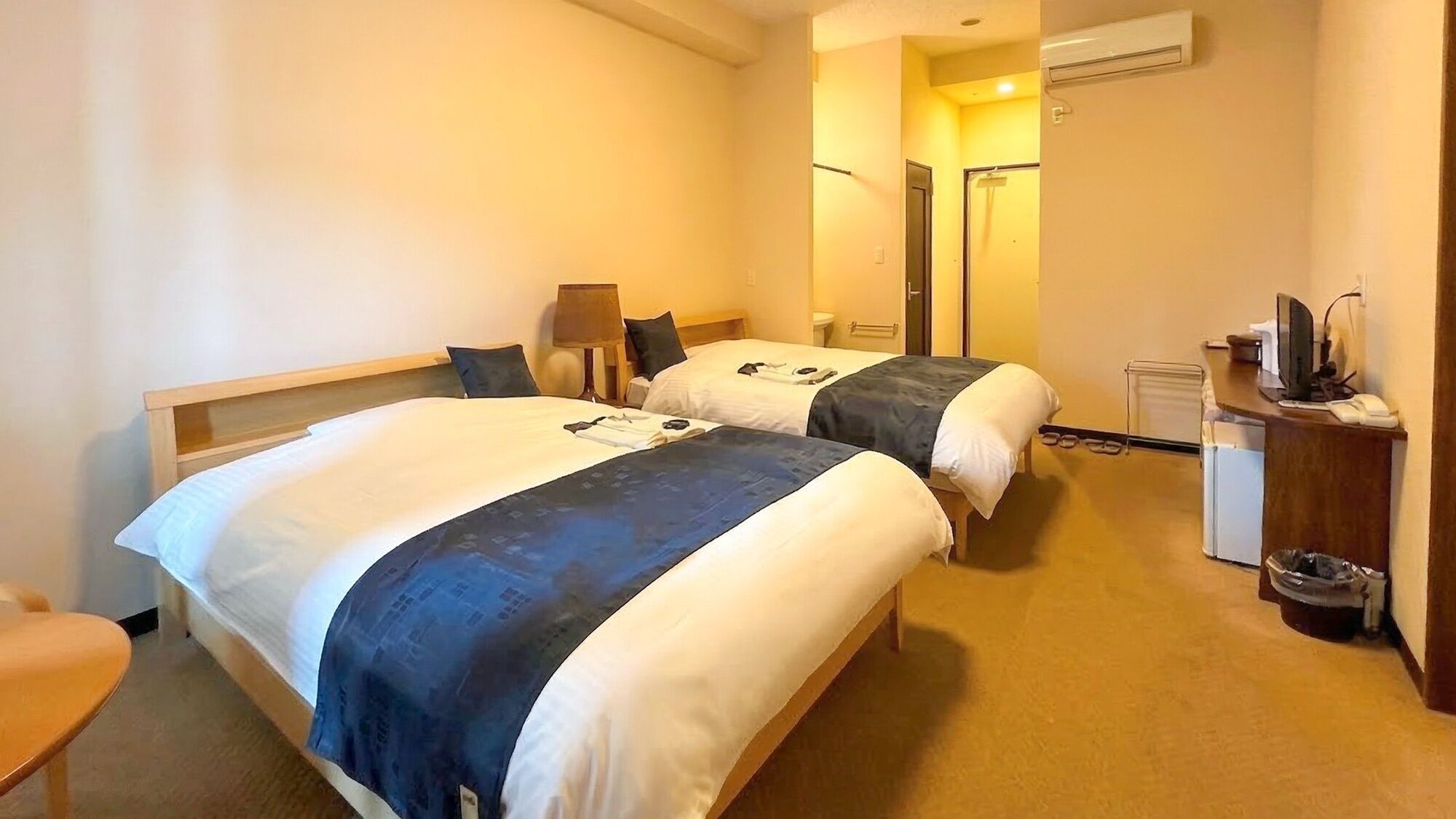 Hotellihuone, jossa on kaksi sänkyä, työpöytä, tuoli ja roskakori.