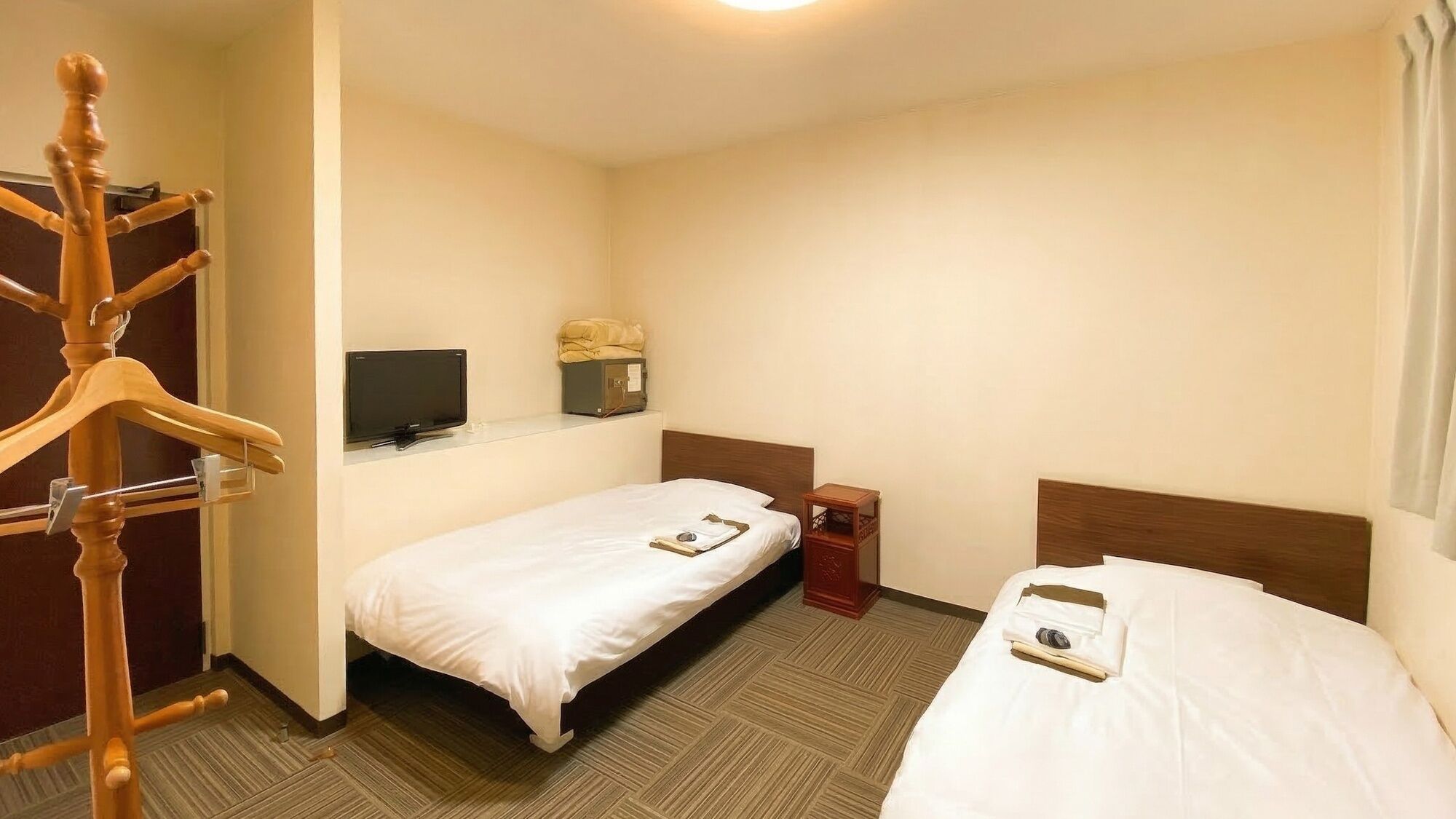Hotellihuone, jossa on kaksi sänkyä, televisio, naulakko ja pieni pöytä.