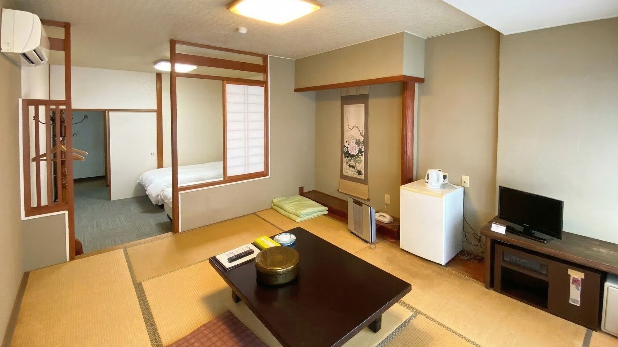Perinteinen japanilaistyylinen huone, jossa on tatamimatto, matala pöytä, jossa on vedenkeitin, televisio ja jääkaappi.