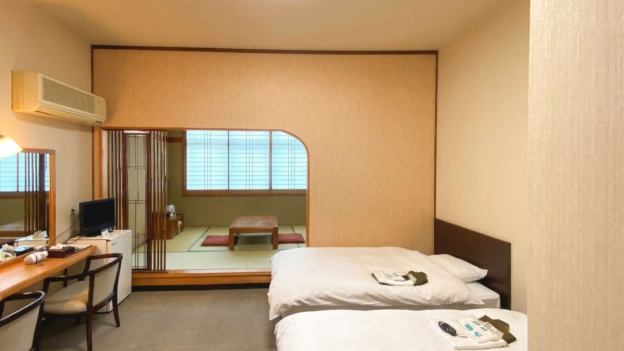 Hotellihuone, jossa on työpöytä, kaksi sänkyä, televisio ja liukuovi, joka johtaa perinteiseen japanilaiseen huoneeseen.