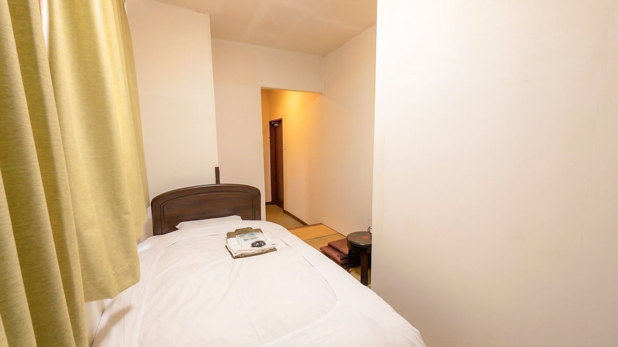 Pieni, kapea hotellihuone, jossa on yksi sänky, yöpöytä ja ovi, joka johtaa käytävään.