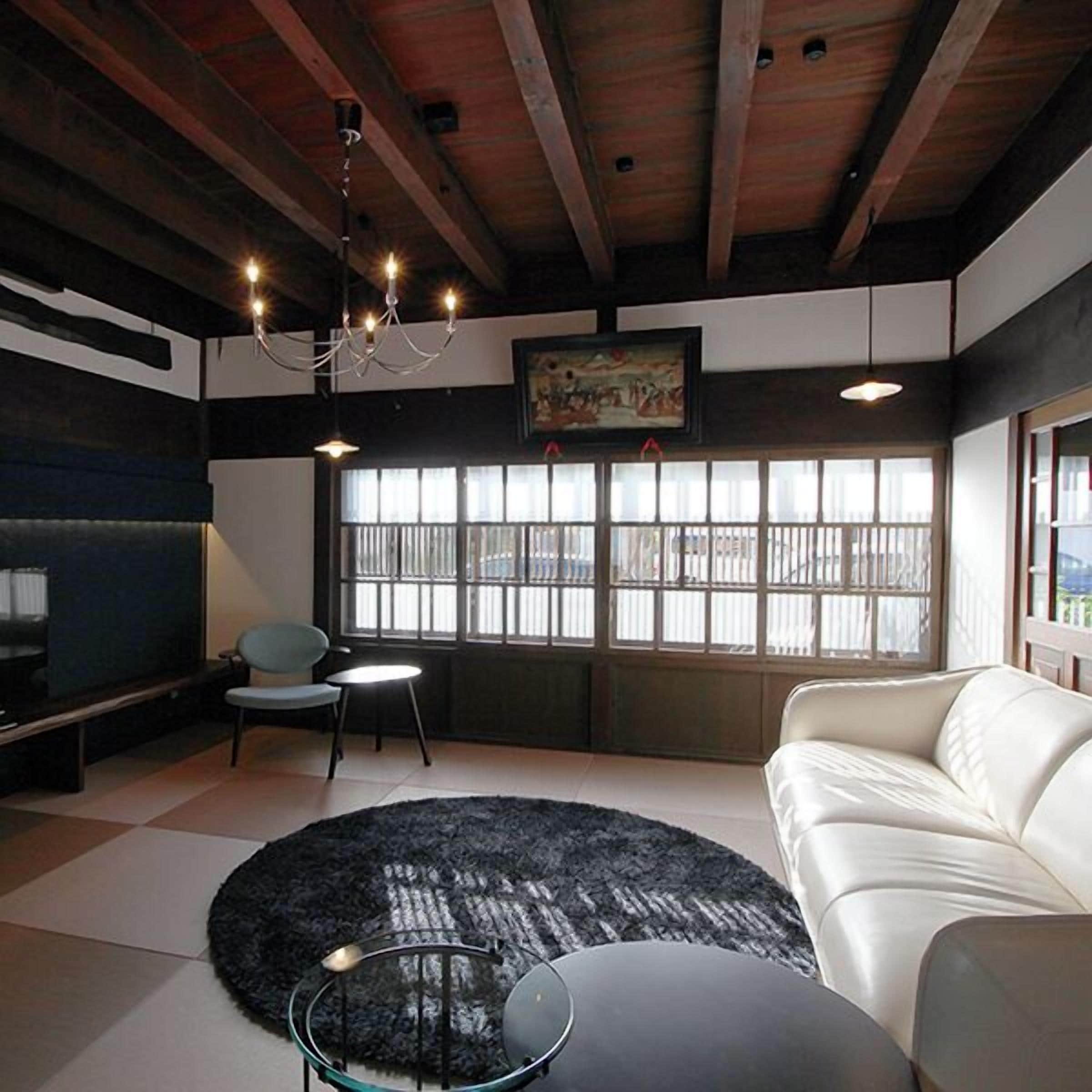 A modern living room with a white sofa, a round black rug, a glass coffee table, a blue chair, and a chandelier.