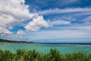 A coastal landscape with clear turquoise waters, a distant shoreline, and a partly cloudy sky. - United Resort Sarabeth (Onna)