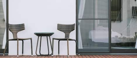 A bench with two wicker chairs and a small table against a white wall with a large window.