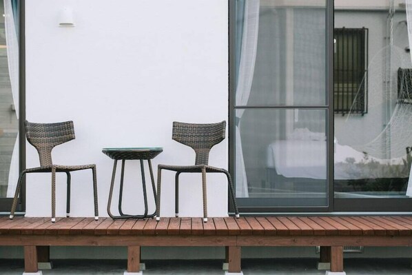 A bench with two wicker chairs and a small table against a white wall with a large window. - United Resort Sarabeth (Onna)
