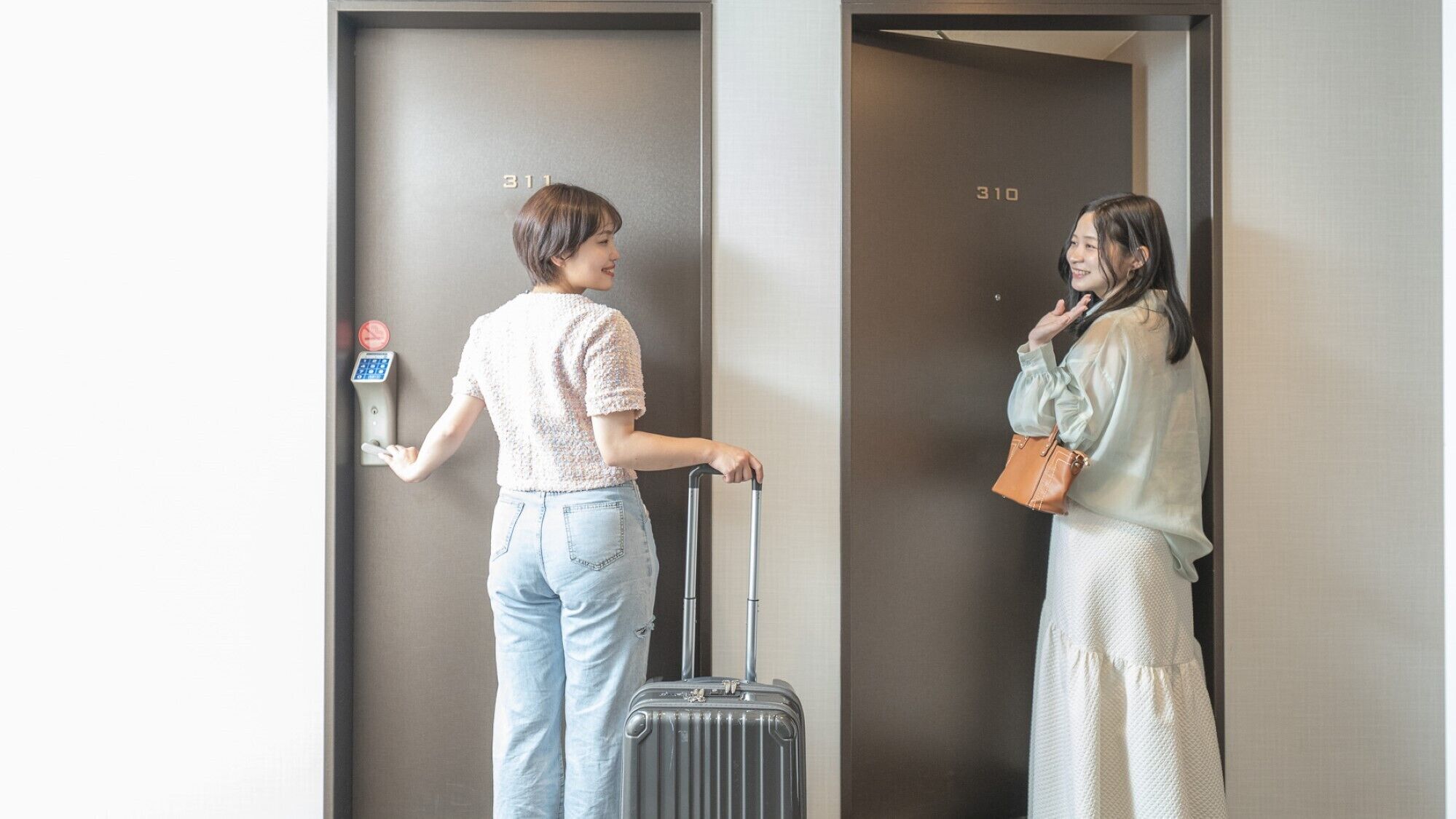 Two individuals in an elevator, one holding a suitcase and a phone, with a digital lock and a keypad on the wall.
