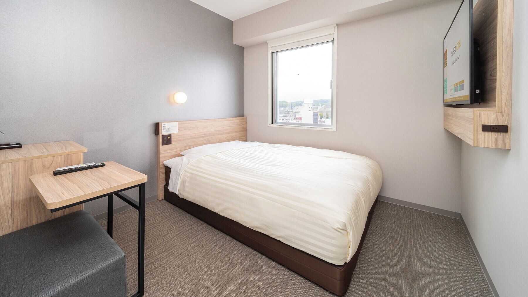 Habitación de hotel con cama, escritorio, silla, televisor montado en la pared y ventana con vista a la ciudad.