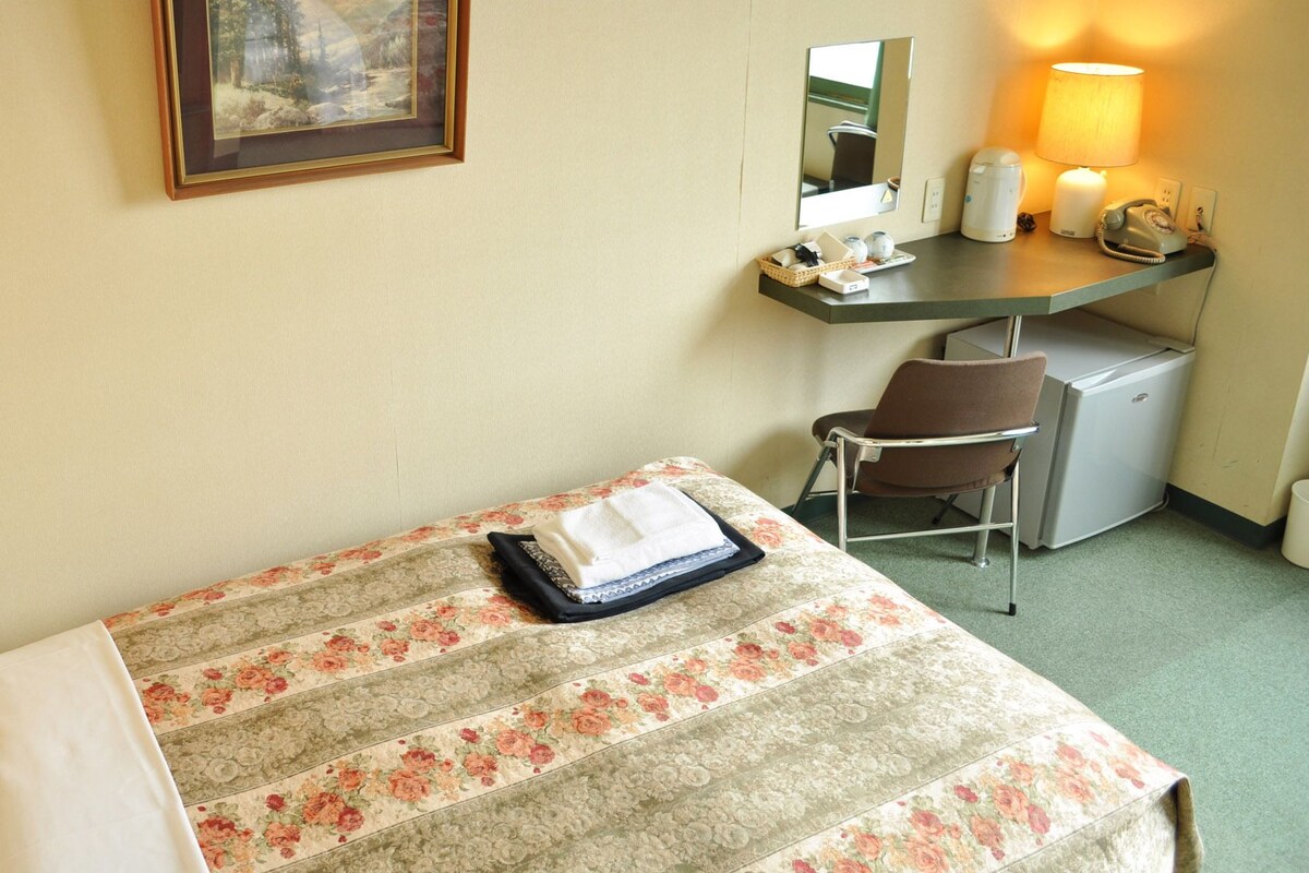 Habitación de hotel con cama, escritorio, silla, refrigerador pequeño, lámpara y teléfono.