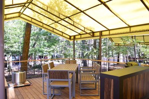 An outdoor patio with a wooden table and chairs, a bar area, and a view of the surrounding forest. - Pica Resort Fuji Yoshida (Fujiyoshida)
