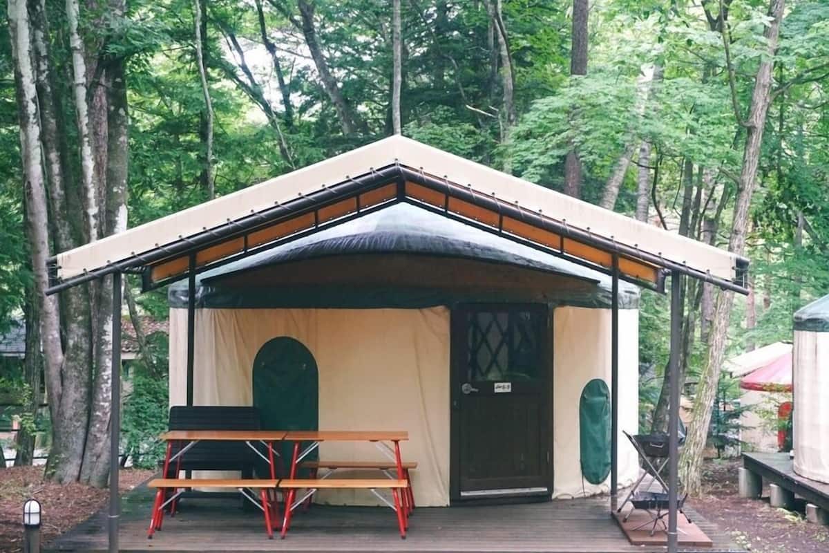 A small, single-room tent with a table and chairs in front, surrounded by trees.