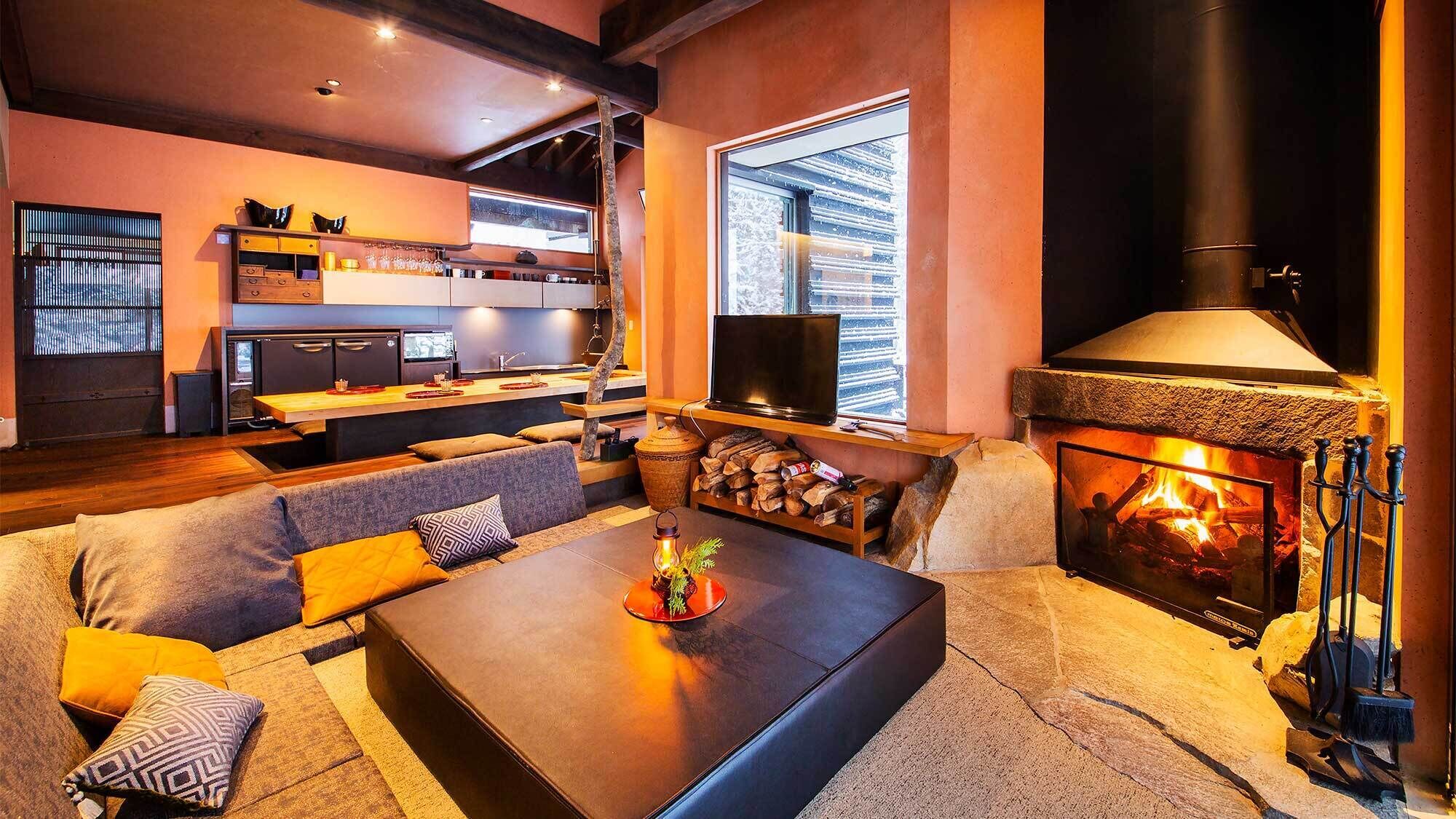 Ein gemütliches Wohnzimmer mit Kamin, einer Couch, einem Couchtisch und einer Küchenzeile mit Fernseher.
