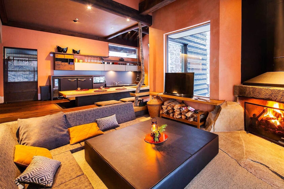 Una sala de estar acogedora con chimenea, un sofá, una mesa de centro y una zona de cocina con televisor.