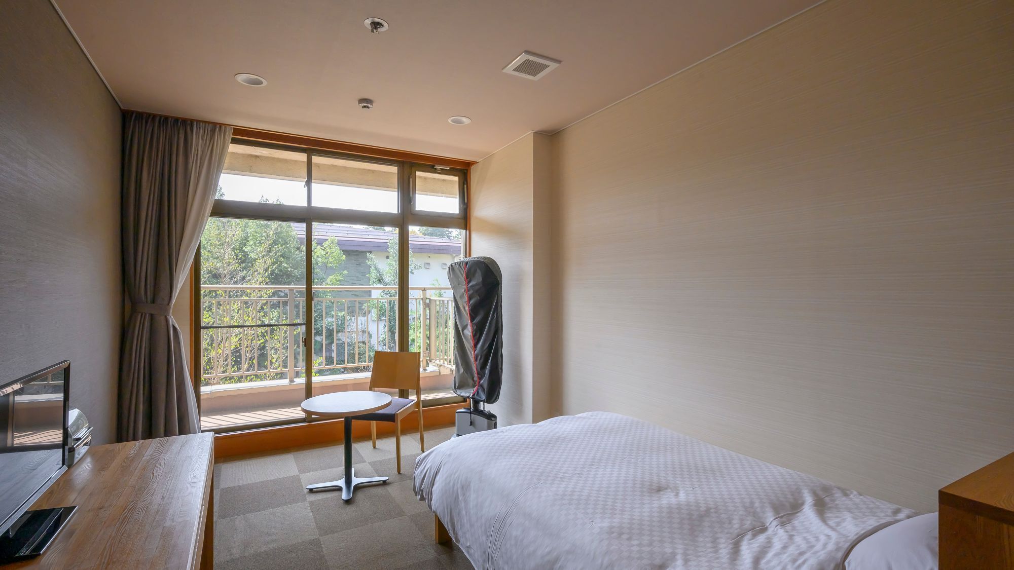 Une chambre d’hôtel comprenant un lit, un bureau avec un ordinateur, une chaise et une fenêtre donnant sur un balcon.