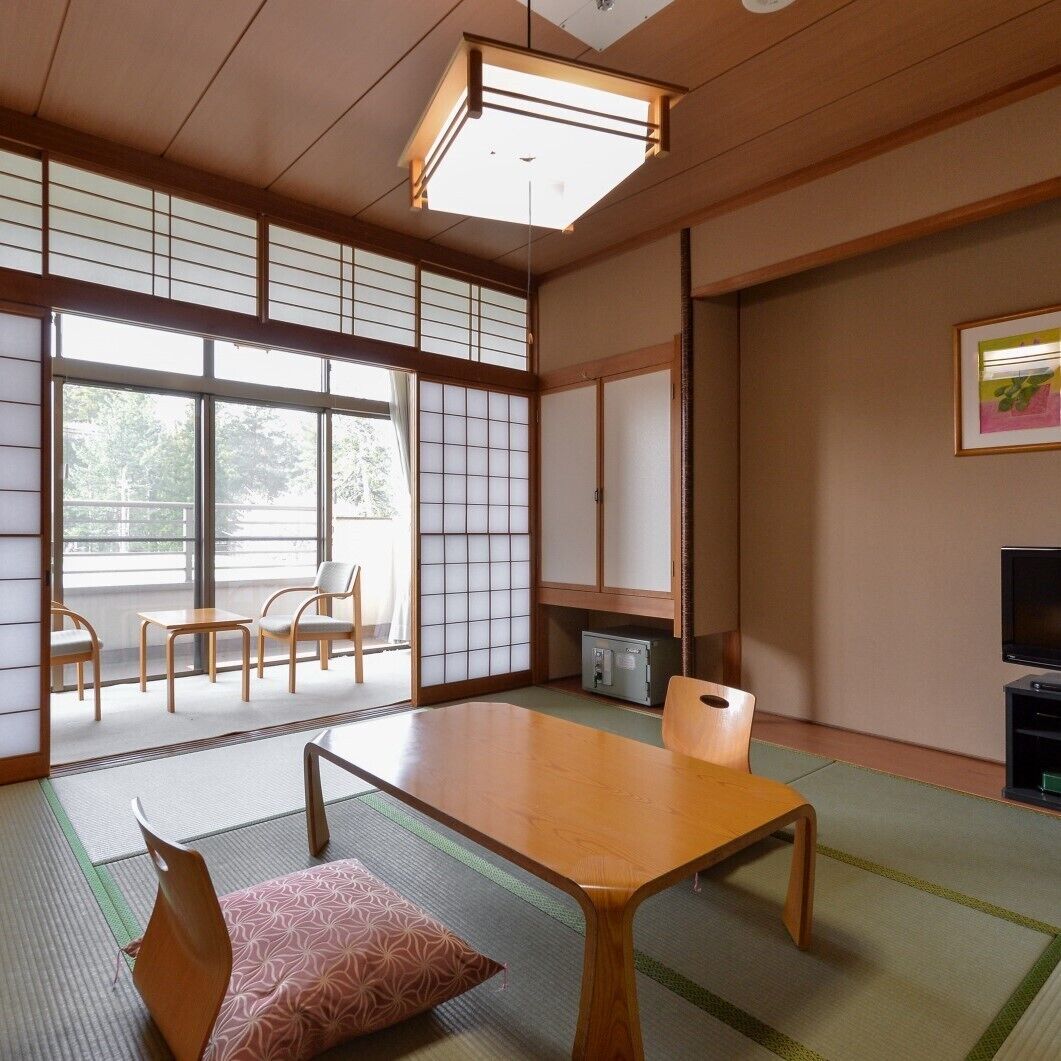 Une pièce de style japonais traditionnel, avec un sol recouvert de tatamis, une table basse, des chaises, un téléviseur et des portes coulissantes.