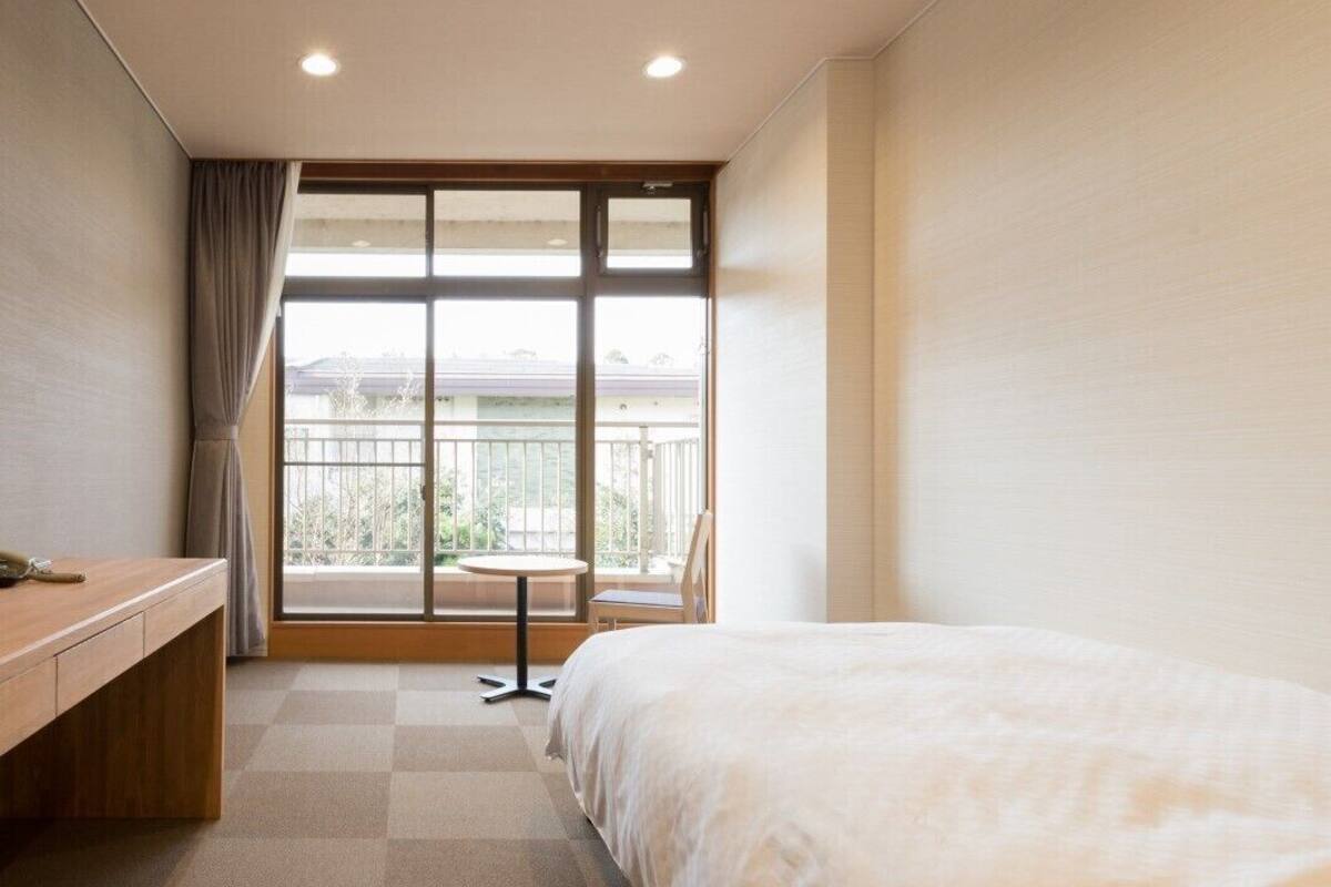 A hotel room with a bed, a desk, a chair, and a balcony with a view.