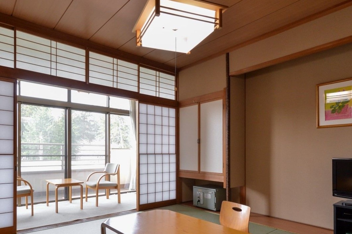 A traditional Japanese room with tatami flooring, a low table, chairs, a television, and sliding doors.