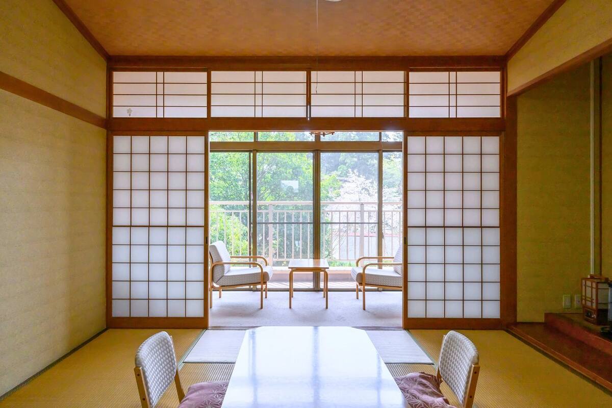 A traditional Japanese room with tatami flooring, a sliding door, and a balcony with a view of greenery.