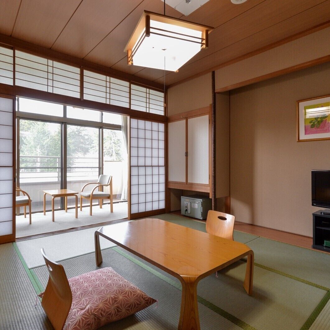 Une pièce de style japonais traditionnel, avec un sol recouvert de tatamis, une table basse, des chaises, un téléviseur et des portes coulissantes.