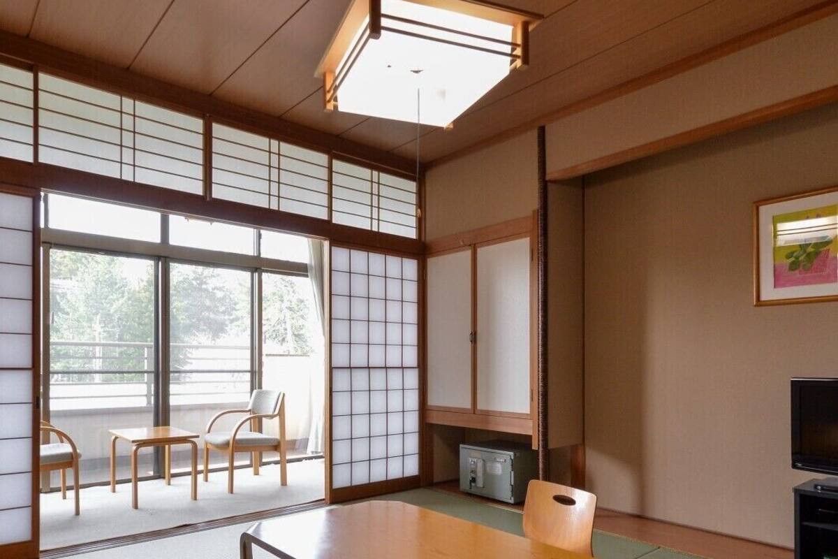 A traditional Japanese-style room with tatami flooring, a low table, chairs, a television, and sliding doors.