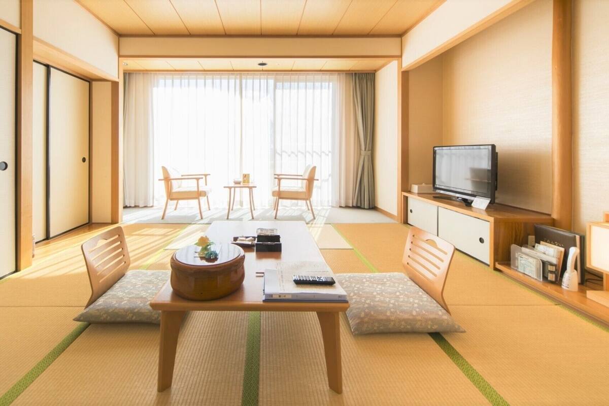 A traditional Japanese-style room with tatami flooring, a low table with cushions, a television, and a sliding door.