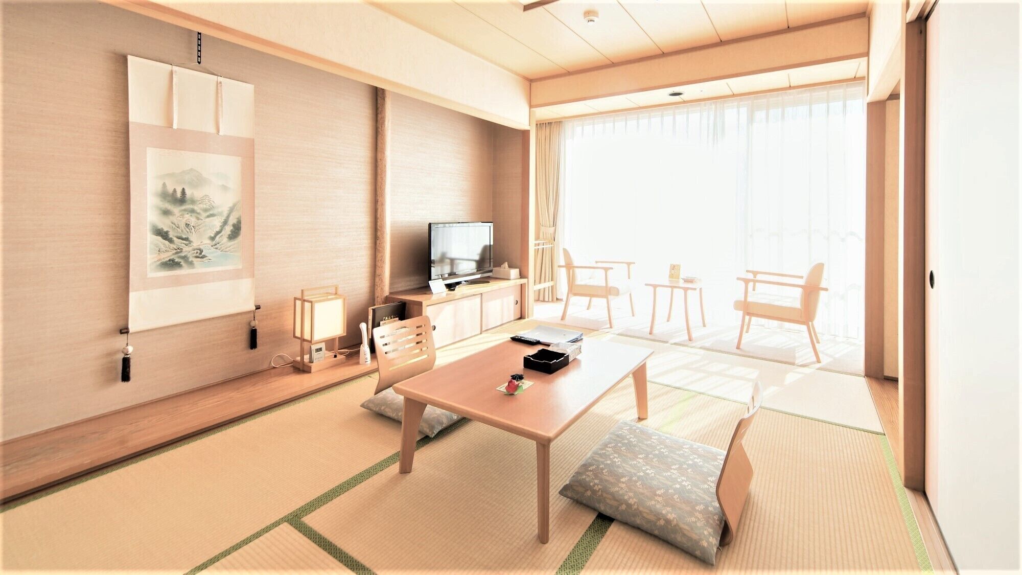 Ein modernes Hotelzimmer mit Holzboden, einem Esstisch, einer Couch, einem Fernseher und einem großen Fenster.