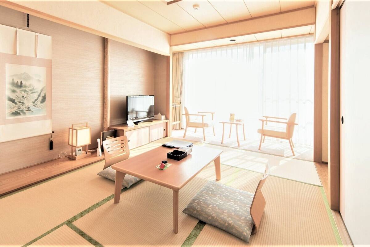 A modern hotel room with a wooden floor, a dining table, a TV, and a balcony with a view.