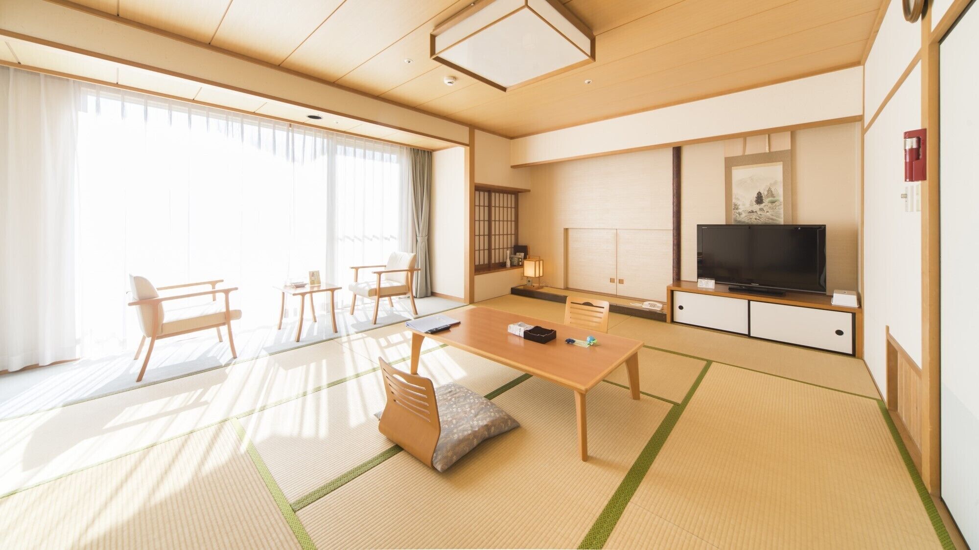 Una habitación tradicional japonesa con suelo de tatami, una mesa baja, sillas, un televisor y una puerta corredera.