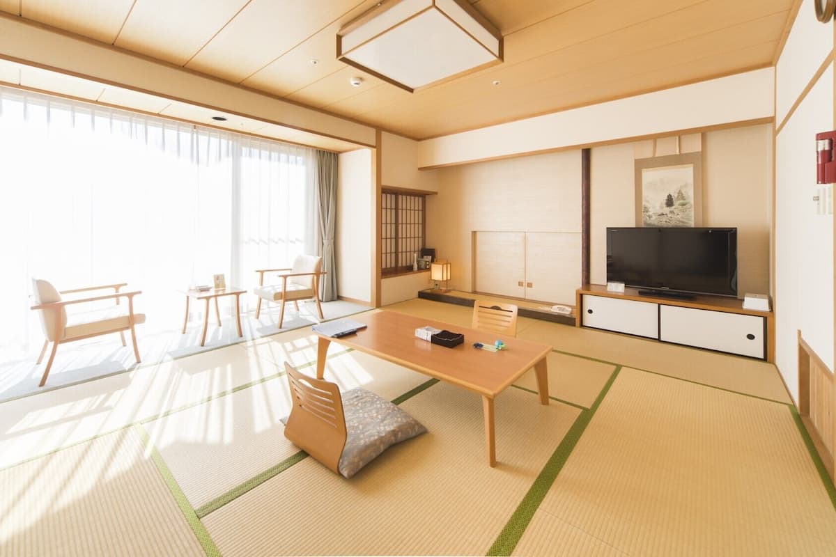 A traditional Japanese-style room with tatami flooring, a low table, chairs, a television, and a sliding door.