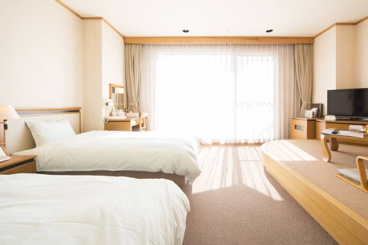 A hotel room with two beds, a desk, a TV, and a chair.