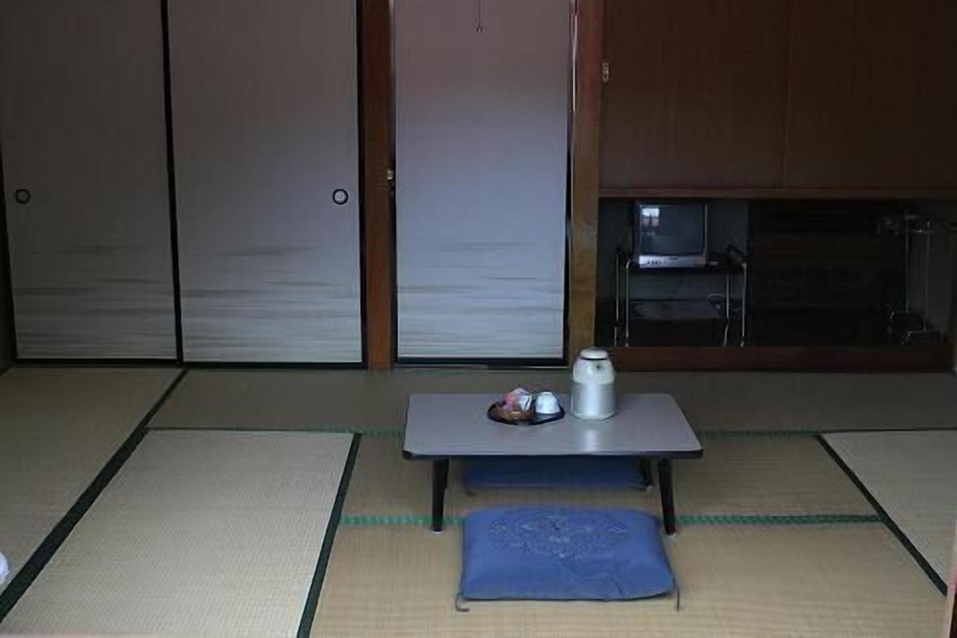 A tatami mat room with a table, a pillow, and a small table with a cup and saucer.