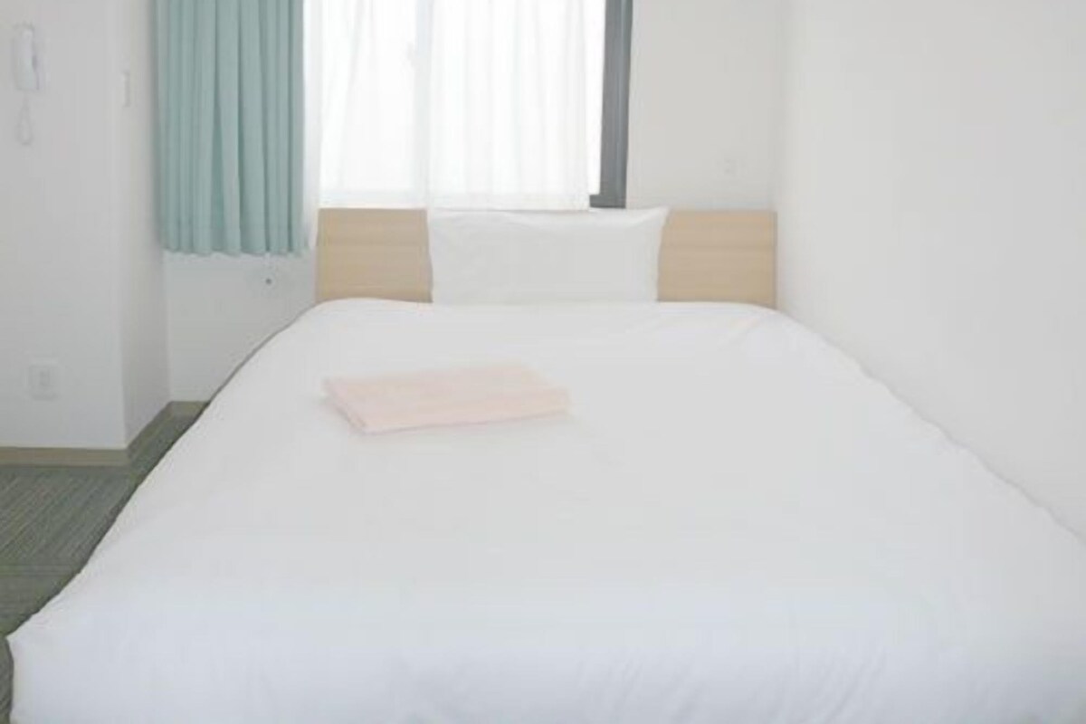 A hotel room with a single bed, a window with curtains, and a bedside table.