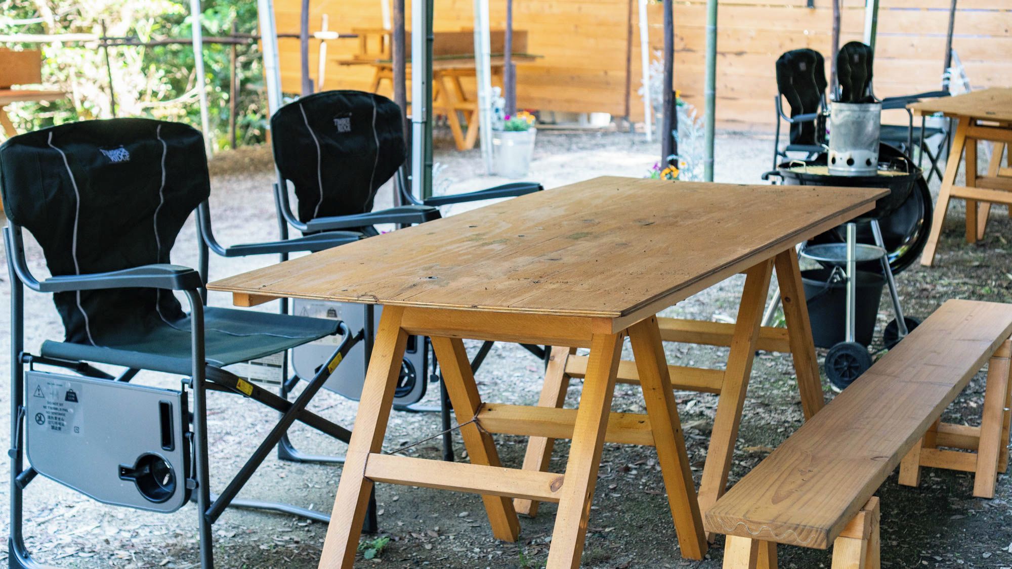 A wooden table with benches, surrounded by black chairs with wheels.