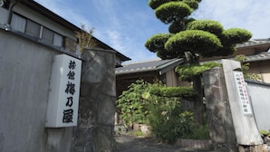 A traditional Japanese building with a stone entrance and a well-maintained garden with bonsai trees. - Ryokan Umenoya (Bungotakada)