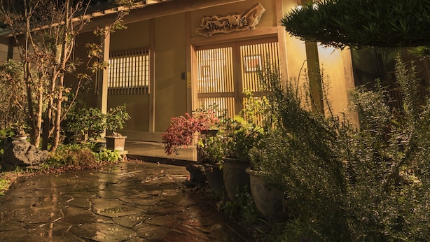 A traditional Japanese-style building with a tiled entrance, wooden doors, and a small garden with potted plants and a stone pathway. - Ryokan Umenoya (Bungotakada)