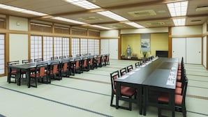 A conference room with long tables and chairs, traditional Japanese sliding doors, and a large window with a view of a mountain. - Ryokan Umenoya (Bungotakada)