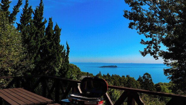 A wooden deck with a barbecue grill and picnic table overlooking a scenic view of the ocean and a distant island. - Atami Kaiun (Atami)