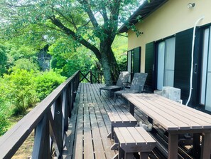 A wooden deck with outdoor seating, surrounded by lush greenery and a large tree. - Atami Kaiun (Atami)