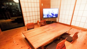 A dining area with a long wooden table, several chairs, and a television on a stand. - Atami Kaiun (Atami)