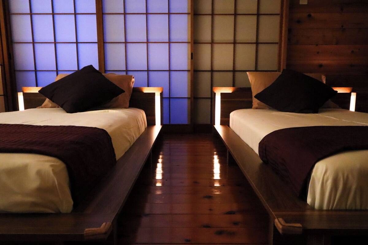 A room with two beds, wooden flooring, and a traditional Japanese shoji screen in the background.