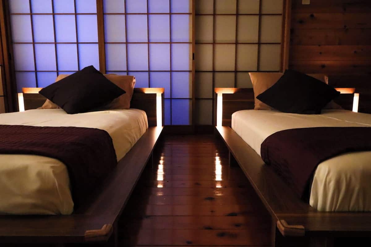 A room with two beds, wooden flooring, and a traditional Japanese shoji screen in the background.