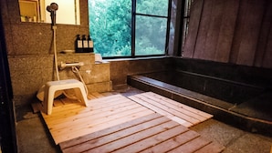 A traditional Japanese-style bathroom with a wooden floor, a small stool, a bathtub, and a window with a view of trees. - Atami Kaiun (Atami)