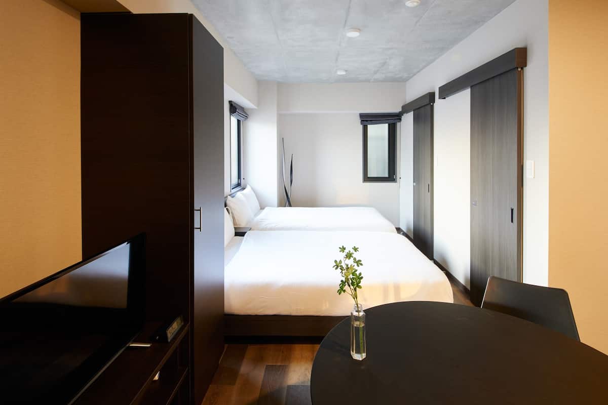 A modern hotel room with a bed, a TV, a dining table, and a vase with a plant.