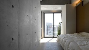 Een slaapkamer met een groot bed, een betonnen muur en uitzicht door een glazen deur.