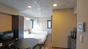 Una habitación de hotel con cama, escritorio con silla, televisor y pequeña kitchenette.