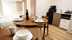 A hotel room with a dining table set for four, a bed, a kitchenette, and a bathroom.