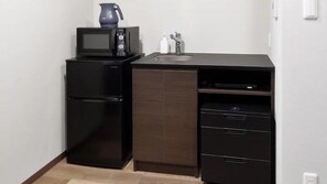Una kitchenette compacta con refrigerador negro, microondas y un lavamanos pequeño.